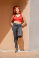 A woman in a red tank top and black pants is standing in front of a wall