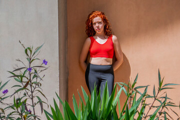 A woman in a red tank top and black pants stands in front of a wall