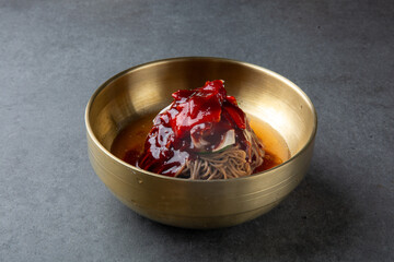 Korean Spicy Buckwheat Noodles in Brass Bowl on Stone Background 놋그릇에 담긴 한국식 비빔 메밀국수