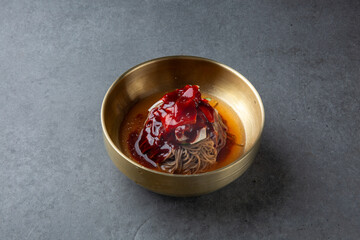 Korean Spicy Buckwheat Noodles in Brass Bowl on Stone Background 놋그릇에 담긴 한국식 비빔 메밀국수