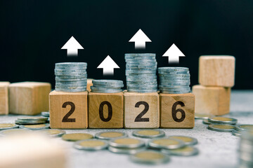 Stack of coins, 2026 wooden text block, and up arrow indicating increase. Financial concept