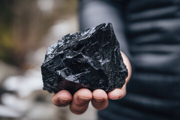 Obsidian volcanic glass shines with glossy black surface in person hand, highlighting natural texture and unique formation of this igneous rock outdoors