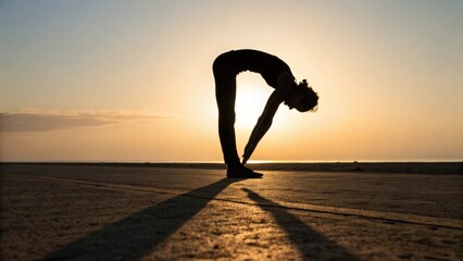 Silhouette of person doing forward bend yoga pose at sunset