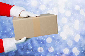 Santa Claus holding parcel on blue gradient background with bokeh lights, closeup. Holiday delivery