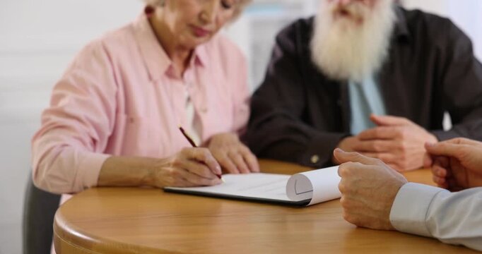 Senior couple signing Last Will and Testament at wooden desk indoors, closeup