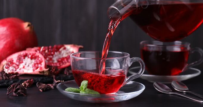 Pouring aromatic pomegranate tea into cup from teapot at dark table, closeup