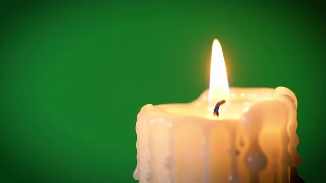 A closeup of a burning candle with a green background