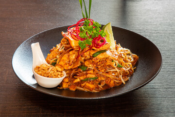 A plate of chicken pad thai with a spoon of peanuts and a pretty garnish top