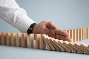 Businessman hand stopping falling wooden dominoes to prevent collapse and manage crisis