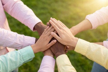Close up of diverse hands stacked together outdoors over green grass symbolizing unity and teamwork