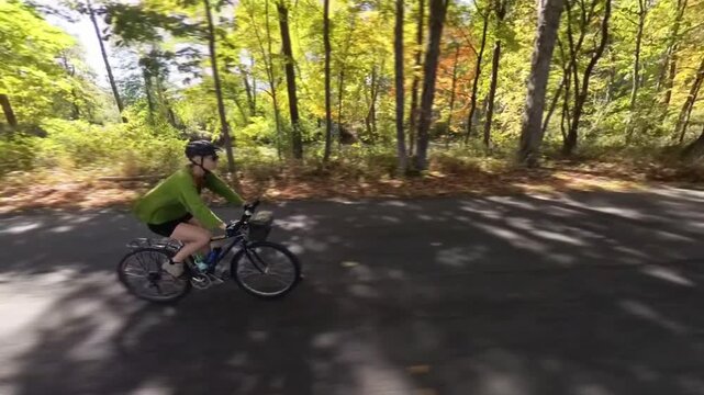 A woman enjoys biking along a beautiful road by the river surrounded by trees in autumn in West Virginia.