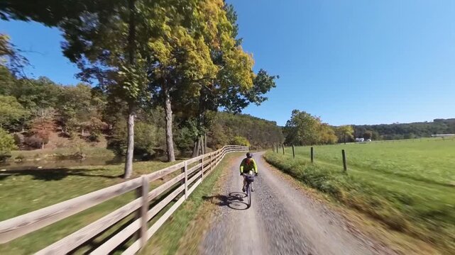A mature woman is biking on a scenic road next to a river in West Virginia on a clear autumn day with colorful trees.