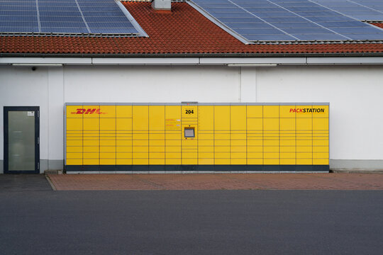 Cologne, Germany June 27 20225: Yellow DHL Packstation automated parcel locker in front of a white building with a red tiled roof and solar panels in Cologne, Germany