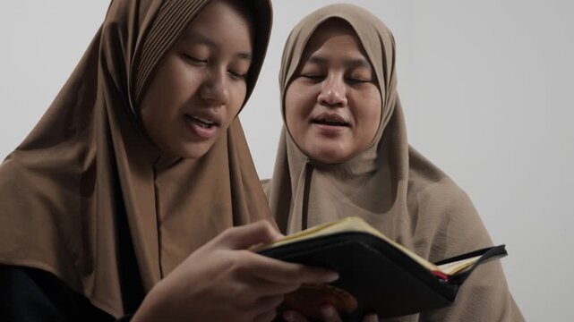 Asian Muslim mother teaching her daughter how to read the Quran at home