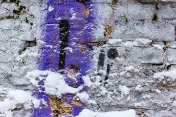 Gritty brick wall texture featuring patches of vibrant purple and black spray paint partially covered in fresh white winter snow