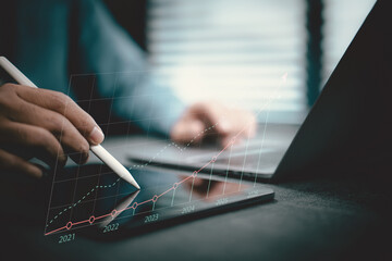 Person Using Stylus to Draw Financial Growth Graph on Digital Tablet with Laptop