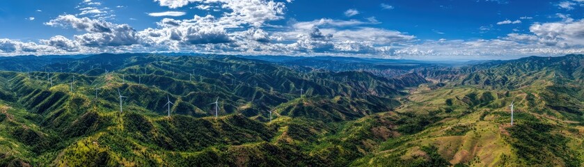 A panoramic view of green hills dotted with wind turbines under a blue sky with clouds, showcasing renewable energy in a natural landscape.