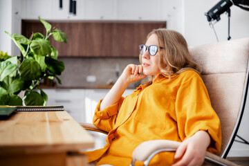 Woman sitting in office chair in glasses with plant and notebook on desk. Focused work atmosphere boosting productivity.