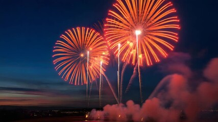 Vibrant orange and red fireworks burst dramatically across the deep twilight sky above a calm body of water creating a spectacular festive celebration - Powered by Adobe