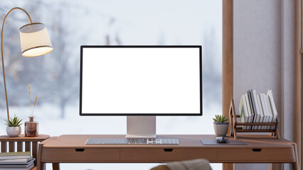 White screen computer with book rack on wooden table aside lamp and snowfall over glass wall window.