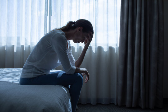 Exhausted  woman in a dark room with head down, Portrait of thoughtful sad female alone. prayer, fear, sadness, abuse, depression, addiction.