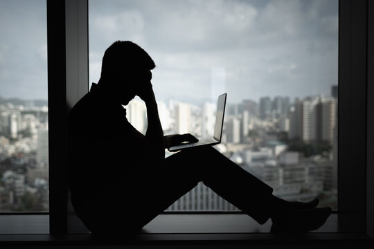 Exhausted stressed man on computer in a dark room with head down, Portrait of thoughtful sad male alone. desperation, , fear, sadness, depression, addiction.