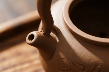 Close-up of a ceramic teapot with a curved spout and handle, resting on a wooden surface.