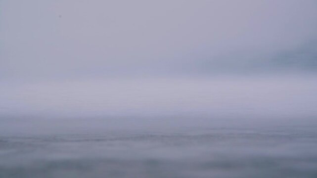A close-up, shallow depth of field, low angle, and slow motion. Snow is blown across the frozen surface of the ice by the wind. An opening shot for a film or video.