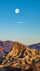 Vast landscape with a moon high in the sky over textured mountains