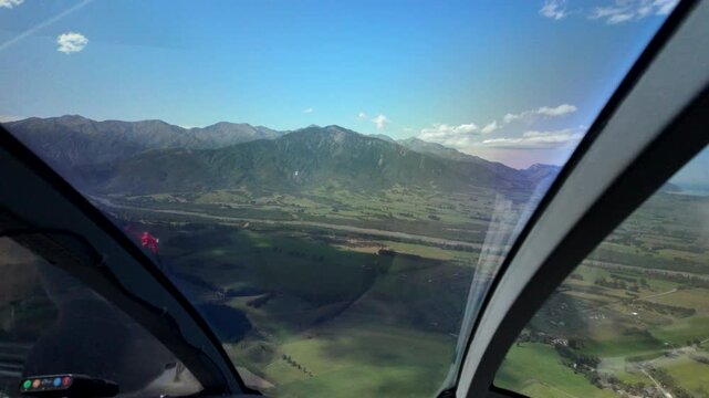 Helicopter cockpit view flying over green valley and mountains