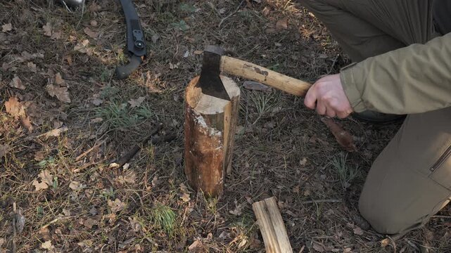 Bushcraft Firewood Splitting With Axe During Forest Survival Preparation, Hands chopping log outdoors using sharp tool beside campsite while practicing wilderness skills