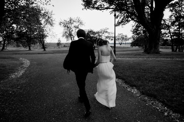 Fototapeta premium Bride and groom walking together along a tree-lined path after their wedding ceremony, captured in timeless black and white with romantic, intimate, and emotional atmosphere.