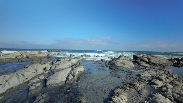 Rocky tide pools and distant surf under clear blue sky