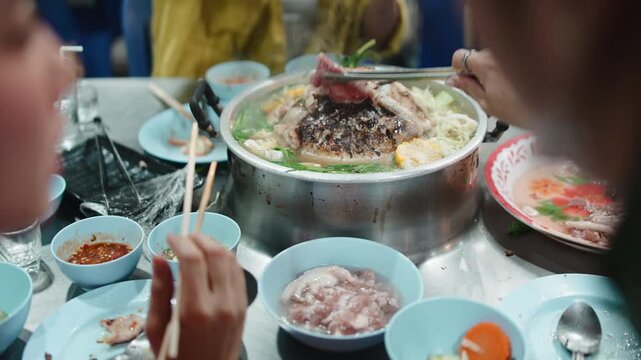 Friends enjoying traditional thai barbecue mookata hot pot dinner