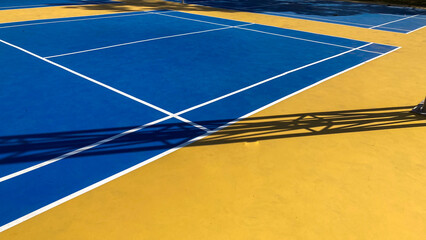 Outdoor Badminton Court with Blue Playing Surface, White Line Markings and Net Casting Pole Shadows in Daylight