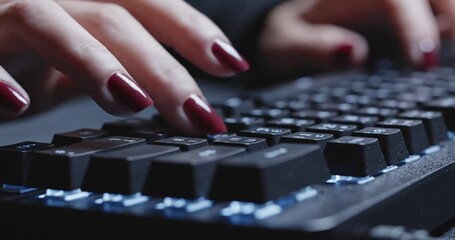 Close-up of a woman's hands typing on a black keyboard with red nails, focused on work