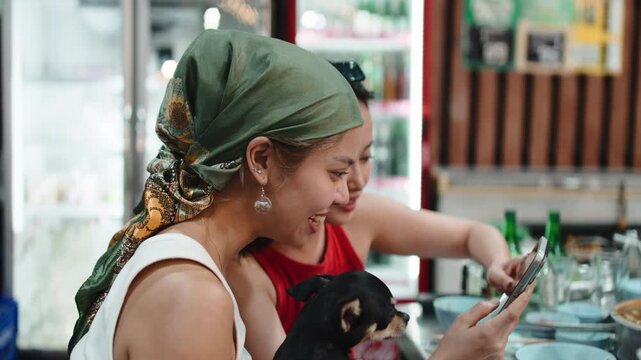 Two cheerful asian women using smartphone at restaurant