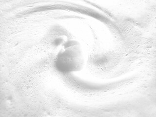 Dynamic high-angle shot of swirling white foam vortex featuring soft motion blur and creamy soap bubbles. Perfect for skincare cleaning or abstract texture backgrounds
