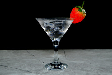 A stylish strawberry martini cocktail served on a black marble coaster, perfect for a luxurious night out or celebration. The refreshing drink features ice cubes and a vibrant strawberry garnish.