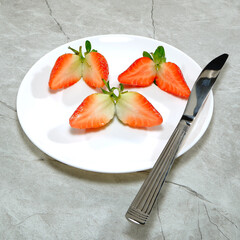 Fresh sliced strawberries on white plate with silver knife closeup view