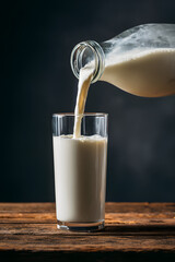 Fresh Milk Pouring from Glass Bottle into Clear Glass on Rustic Table