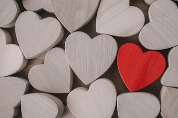 Obraz premium One Red Heart Standing Out Among Many Natural Wooden Heart Shapes for Unique Love Concept