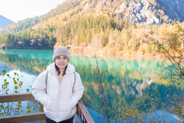 Fototapeta premium Happy woman traveler travel in jiuzhaigou national park in Sichuan, China. Tourist sightseeing Arrow Bamboo lake and snow mountain in Autumn season. Famous Landmark and Vacation near Chengdu, China