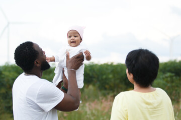 Family with child holding colorful pinwheel near wind turbines.