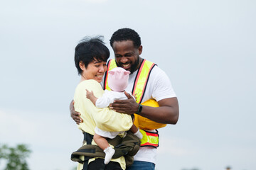 Working father in safety vest holding baby with mother outdoors.