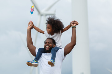 Father and daughter with colorful pinwheel near wind turbines. Renewable energy and sustainability concept.