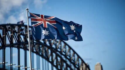 The Australian flag waving gracefully as the Sydney Harbour Bridge arches across a clear blue sky in the background - Powered by Adobe
