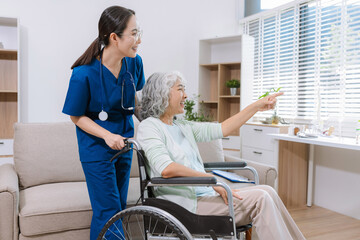 Fototapeta premium Smiling physiotherapist taking care of the happy senior patient in wheelchair at home.