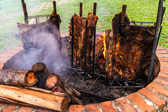 Traditional gaucho barbecue in Brazil: beef ribs slow-roasting vertically on iron frames over a wood-fueled open fire, yielding smoky, tender meat and showcasing rural culinary heritage.