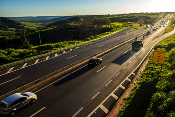 Marilia, SP, Brazil, November 19, 2025. Highway SP-294 in Marilia, at sunset. Intense traffic of cars and trucks flows through the green landscape, illuminated by the golden hour light.